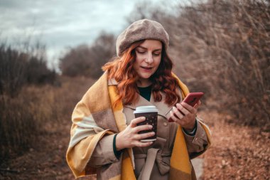 Akıllı telefon kullanan ve kahve servisi yapan güzel genç bir kadın.