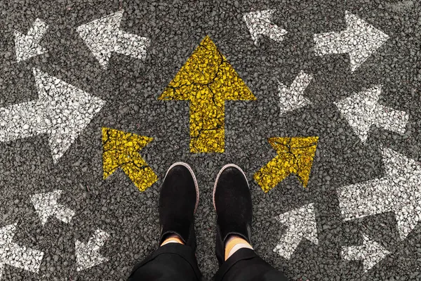 Person standing on road with arrow markings pointing in different directions or pathway, decision making concept. Top view.