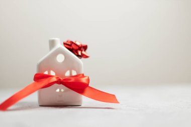 Noel ve yeni yıl tatili. Beyaz arka planda kırmızı saten kurdeleli minyatür beyaz oyuncak ev. Düz konum, üst görünüm, kopyalama alanı