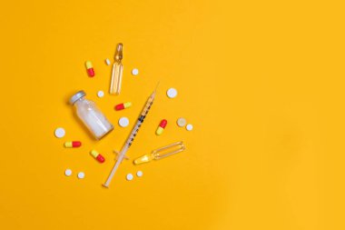 Aşı ve şırınga, çeşitli ilaç hapları, tabletler ve kapsüller sarı arka plan. Sağlık ve Tıp Konsepti.