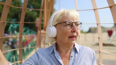 Beyaz, mutlu, 50 'li yaşlarda kadın yüzü. Akıllı telefon kullanıyor ve kulaklıkla sokak ortasında müzik dinliyor. Kentsel yaşam tarzı kavramı