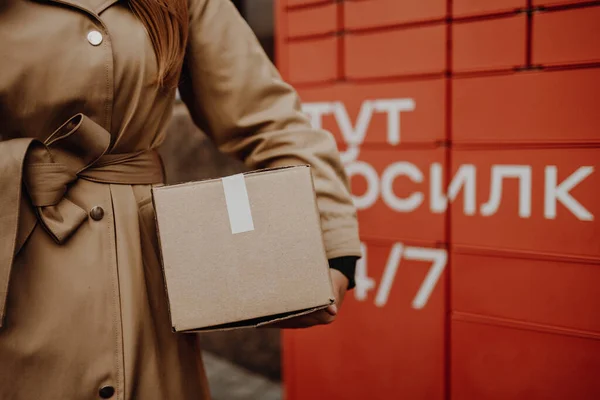 Young caucasian woman picks up mail from automated self-service post terminal machine.