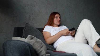 Uzaktan kumandayı elinde tutan kadın. Oturma odasındaki akıllı televizyonu aç..