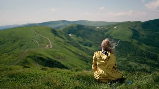 Mulher turista viagem bonita em uma capa de chuva amarela sentado no topo do monte de manhã. Montanhas Cárpatas na Ucrânia. Temporada de verão. Caminhada, turismo — Vídeo de Stock