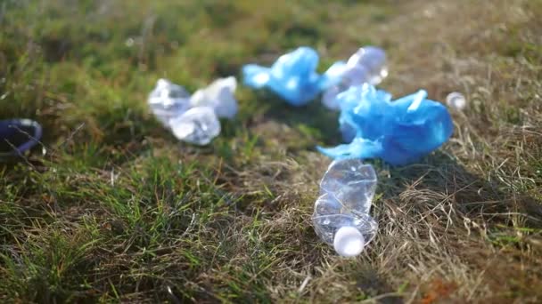 Giovane volontaria donna in guanto di gomma blu protettivo che raccoglie immondizie in campo autunnale, bottiglia di plastica blu primo piano, pacchetti sdraiati a terra — Video Stock