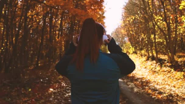Beyaz kablosuz kulaklıklı aktif kadın sonbahar orman parkında koşuyor. Arkadan bak. Spor, refah ve spor kızı konsepti — Stok video