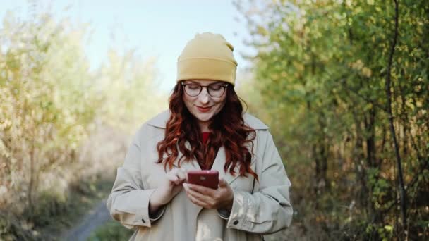 Video de una mujer joven disfrutando de viajar y usar el teléfono móvil en un parque de otoño de la ciudad — Vídeos de Stock