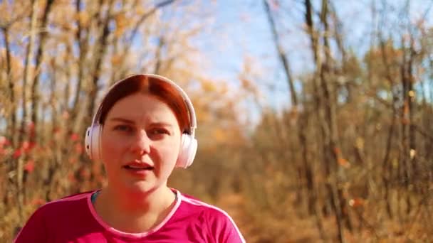 Ενεργό τρέξιμο γυναίκα με λευκά ακουστικά τρέχει στη φύση autimn πτώση. Γυμναστική έννοια υγιεινό τρόπο ζωής. — Αρχείο Βίντεο