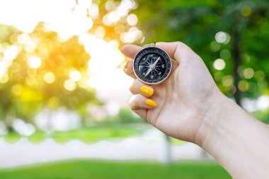 Yeşil arka planda pusulalı bir el, gün batımında güneş parlıyor.