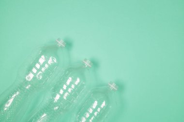 Kullanılmış plastik şişeler geri dönüşüm için yeşil arka planda kaotik bir şekilde yatar. Üst görünüm, alanı kopyala.