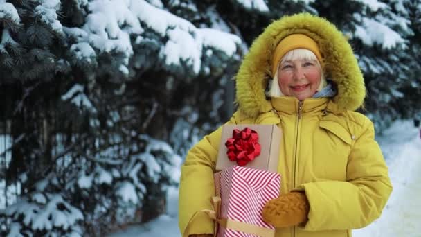 正白人50代女性で黄色服手保持ギフトボックスと手を振ってクリスマスショッピングで屋外で市. — ストック動画