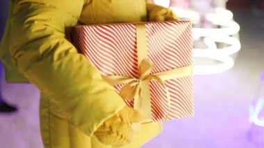 Kadın eli hediye kutusunu tutuyor ve gece caddesinde duruyor. Xmas çelenk dekorasyonu. Noel ve Yeni Yıl alışverişi, satış konsepti