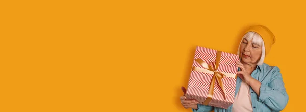 Retrato de bastante maduro años 50 mujer arco de vacaciones caja de cinta sosteniendo en las manos sobre fondo de color amarillo —  Fotos de Stock
