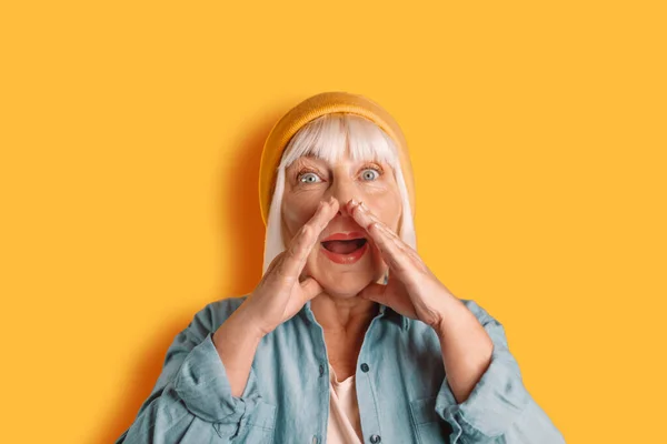 A cheerful woman in her 50s poses isolated against a yellow and orange background. Screaming and holding her hands near her face — Fotografia de Stock