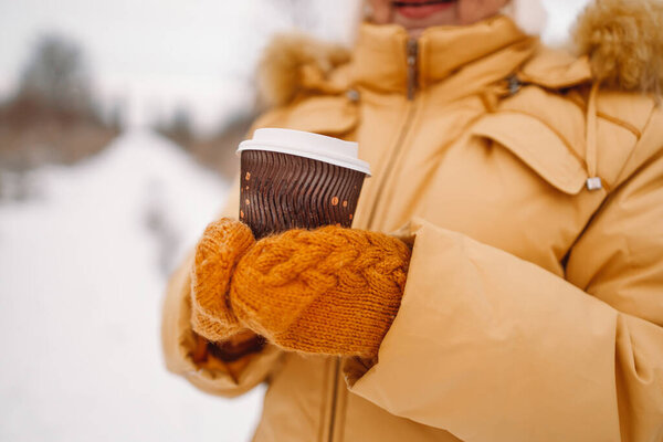 Female hand is holding paper coffee cup outdoors at winter cold frosty snowy day. Winter holidays