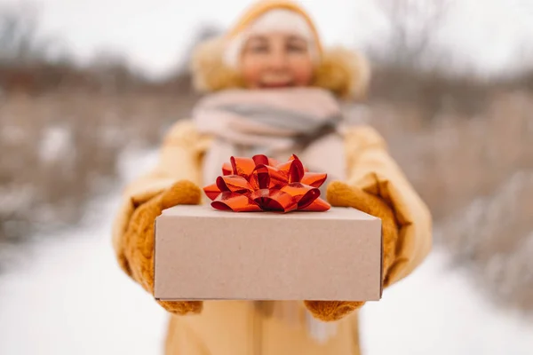 Atrakcyjny podekscytowany uśmiechnięta młoda kobieta trzyma pudełko prezentów w rękach i patrzy na aparat w zimowy mroźny śnieżny dzień — Zdjęcie stockowe