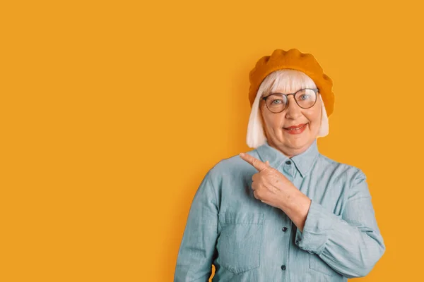 Beautiful middle aged caucasian woman in glasses and stylish clothes smiling shows question pointing finger up good mood isolated over bright orange color background — Fotografia de Stock