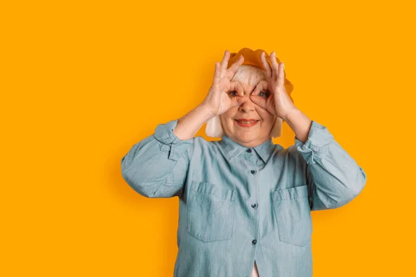Friendly 40s 50s caucasian woman and stylish clothes having fun making glasses shape with hands isolated over bright orange color background — Fotografia de Stock
