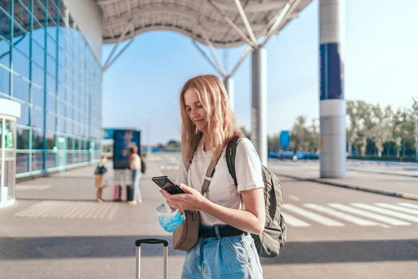 Toeristische reiziger meisje met rugzak en koffer maakt gebruik van een mobiele smartphone in de buurt van de internationale luchthaven — Stockfoto