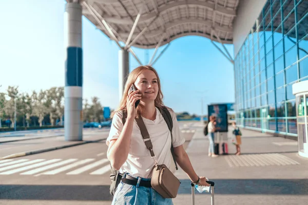 Toeristische reiziger vrouw met rugzak en koffer praten op een mobiele smartphone in de buurt van de internationale luchthaven — Stockfoto