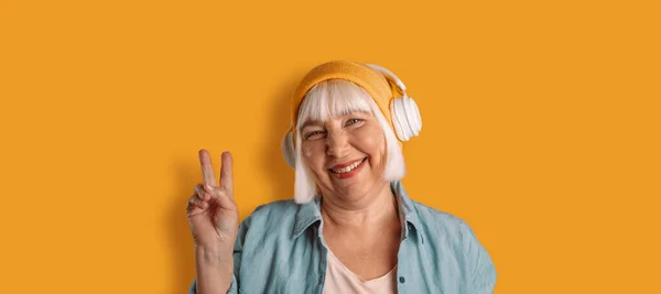 Happy 50s woman listens music expresses sincere emotions being in good mood isolated over yellow background. Joy concept — Fotografia de Stock