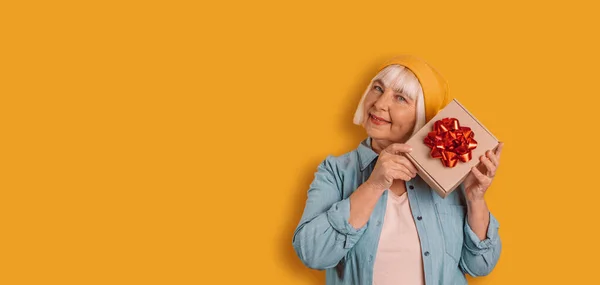 Retrato de atractiva alegre divertida mujer de los años 50 sosteniendo abrazo regalo en las manos regalo buen humor aislado sobre fondo de color naranja brillante —  Fotos de Stock