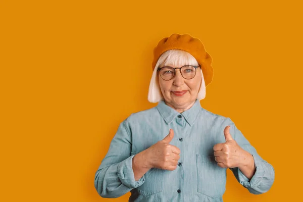 Portrait of caucasian 50s woman showing thumbs up good mood in studio isolated over bright orange color background — Fotografia de Stock