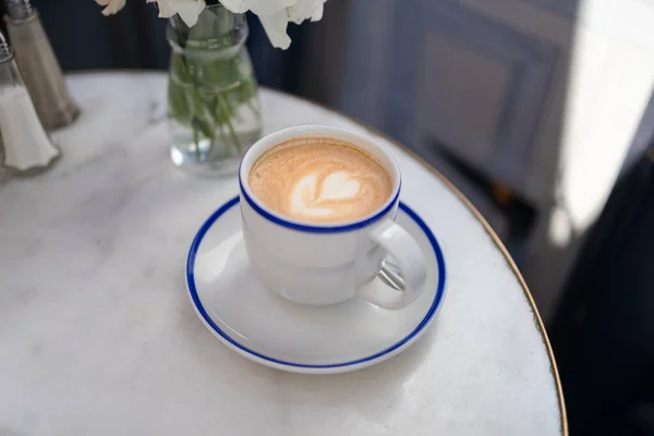 Copa de vidrio de capuchino café caliente en la mesa de mármol blanco en la cafetería de la calle, café por la mañana —  Fotos de Stock