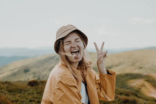 Portait ξέγνοιαστες νεαρή ξανθιά γυναίκα κάνει την πινακίδα νίκη στην κορυφή του βουνού σε μια ηλιόλουστη μέρα του καλοκαιριού. — Φωτογραφία Αρχείου