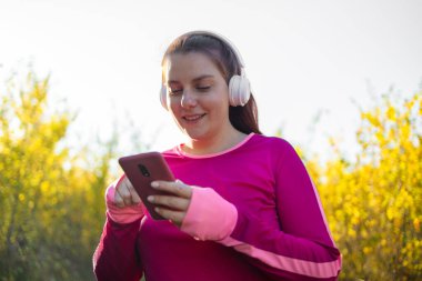 Fitness kadın koşucusu dışarıda koşuyor kulaklıkla akıllı telefondan müzik dinliyor. Sonbahar doğa koşusu yapan bayan fitness kızı..