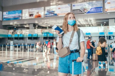 Uluslararası havaalanında pasaportu olan koruyucu maskeli mutlu genç turist kadın. Covid-19 salgınından sonra seyahat