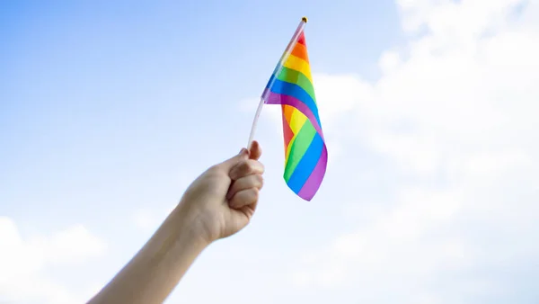 Społeczność LGBT. Mała flaga lgbt w dłoni przeciwko błękitnemu niebu — Zdjęcie stockowe
