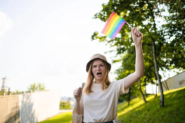 Beautiful caucasian lesbian woman smiling and holding rainbow flag during pride parade walking on city street — Fotografia de Stock