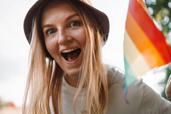 Hermosa mujer lesbiana caucásica sonriendo y sosteniendo la bandera del arco iris durante el desfile del orgullo —  Fotos de Stock