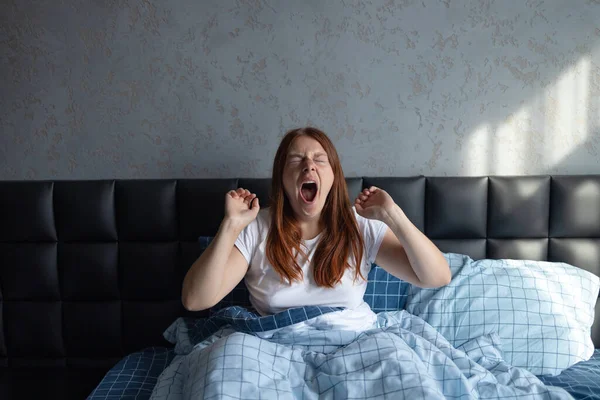 Joven mujer bonita bostezar y estiramiento cubierto con manta blanca en la cama cómoda en casa. —  Fotos de Stock