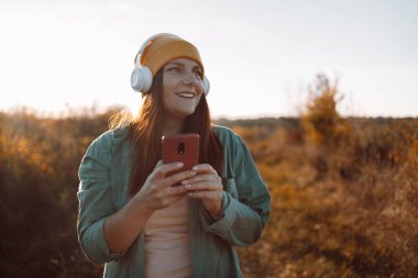 Happy beautiful young caucasian woman listening music with headphones on sunny day while walking in city park