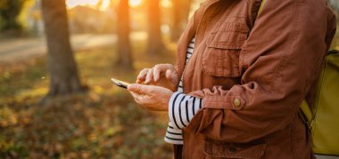 Woman hand holding mobile phone checks messages and reads news in autumn nature field at sunset
