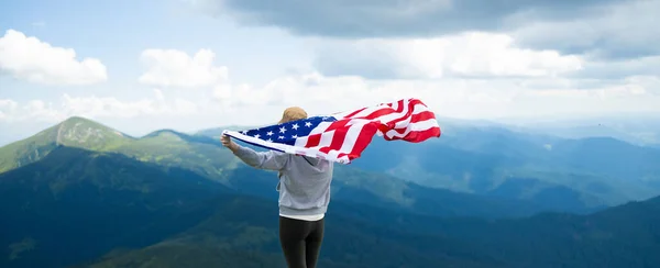 Kobieta wspinaczka stojąca duży sztandar USA amerykańska flaga na szczycie góry — Zdjęcie stockowe