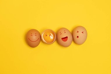 Brown chicken eggs and one broken egg with yolk on yellow background
