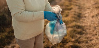 Earth day. Female activist hand puts a plastic bottle trash in a garbage bag.