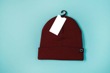 Mavi arkaplan üzerinde boş beyaz etiket mokapağı ve kopyalama alanı olan ılık yün örülmüş şapkanın düz uzantısı