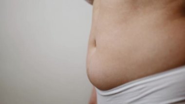 Şişman kadın bej arka planda izole edilmiş fazla yağ çıkarmak için ellerini kullanıyor..