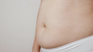 Beyaz arka planda şişko göbeğini tutan tanınmayacak kadar şişman bir kadının yakın çekimi..
