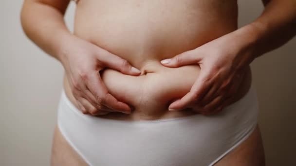 Крупный план обрезаны неузнаваемым плюс размер толстой женщины рука держит жир живота на белом фоне. — стоковое видео