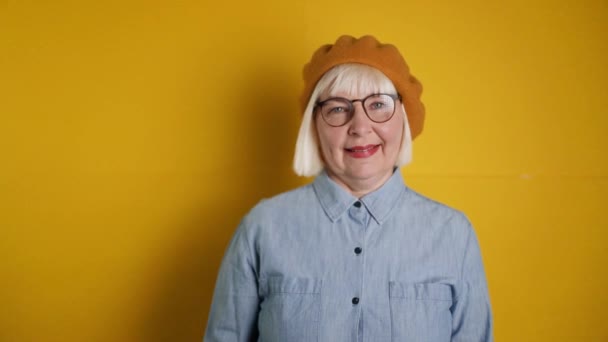 Beautiful middle aged caucasian woman in glasses and stylish clothes smiling shows question pointing finger up good mood isolated over bright orange color background — Stock Video