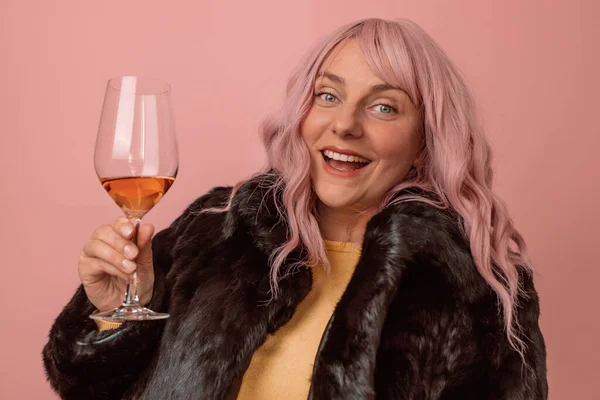 冬の衣装を着たかなり若い女性の肖像と隔離されたピンクの背景にシャンパンとガラスを保持 — ストック写真