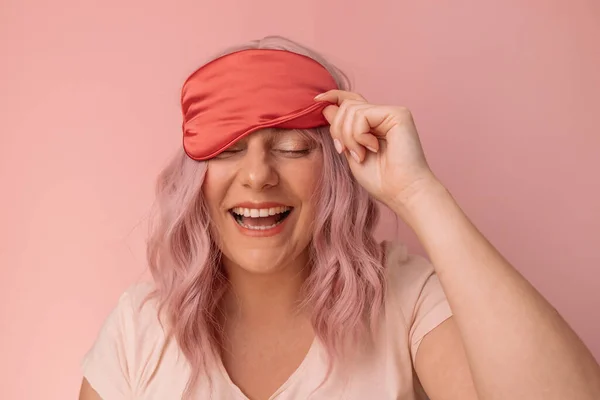 ハッピー女性でパジャマ笑顔歯に取る赤い絹の睡眠マスク楽しんで朝時間 ポーズ隔離されたピンクの背景 — ストック写真