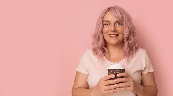 年轻美丽的20多岁的女人穿着白色T恤 拿着外卖咖啡杯 带着粉红的背景微笑 案文的篇幅 — 图库照片