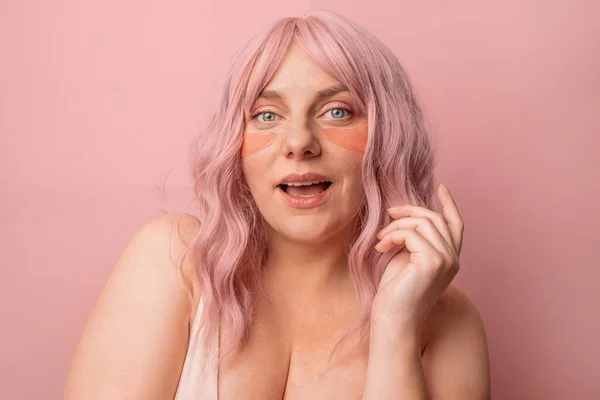 ピンクの背景の上に孤立した眼帯の下にピンクを適用する美しい女性 スキンケア — ストック写真