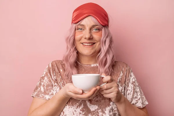 幸せな笑顔魅力的な女性保持していますAカップの香りのコーヒーや紅茶で午前中に隔離されたピンクの背景 — ストック写真